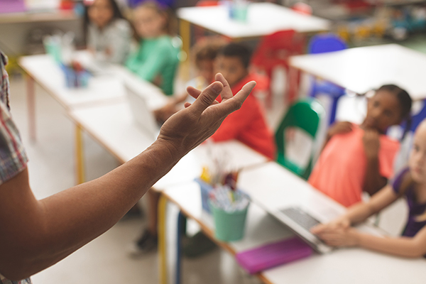 close-up-of-teacher-arm-against-blur-school-kids